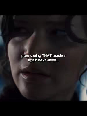 A close-up shot from the movie 'The Hunger Games'. The image focuses on the face of a character, likely Katniss Everdeen. The character is looking slightly to the side with a soft, contemplative expression. The lighting is dim, creating shadows that enhance the character's facial features and the overall mood of the scene. The background is blurred, suggesting a focused shot on the character's face.
