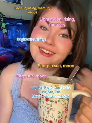 A woman with fair skin smiles while holding a coffee mug. Text overlays indicate astrological signs and placements around her face and on the mug.