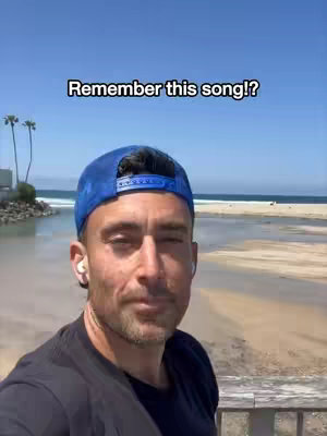 A man wearing a backwards blue cap and black shirt stands in front of a beach scene with a blue sky. The upper part of his face is the focus of the image, with a text overlay that reads 'Remember this song!?' 