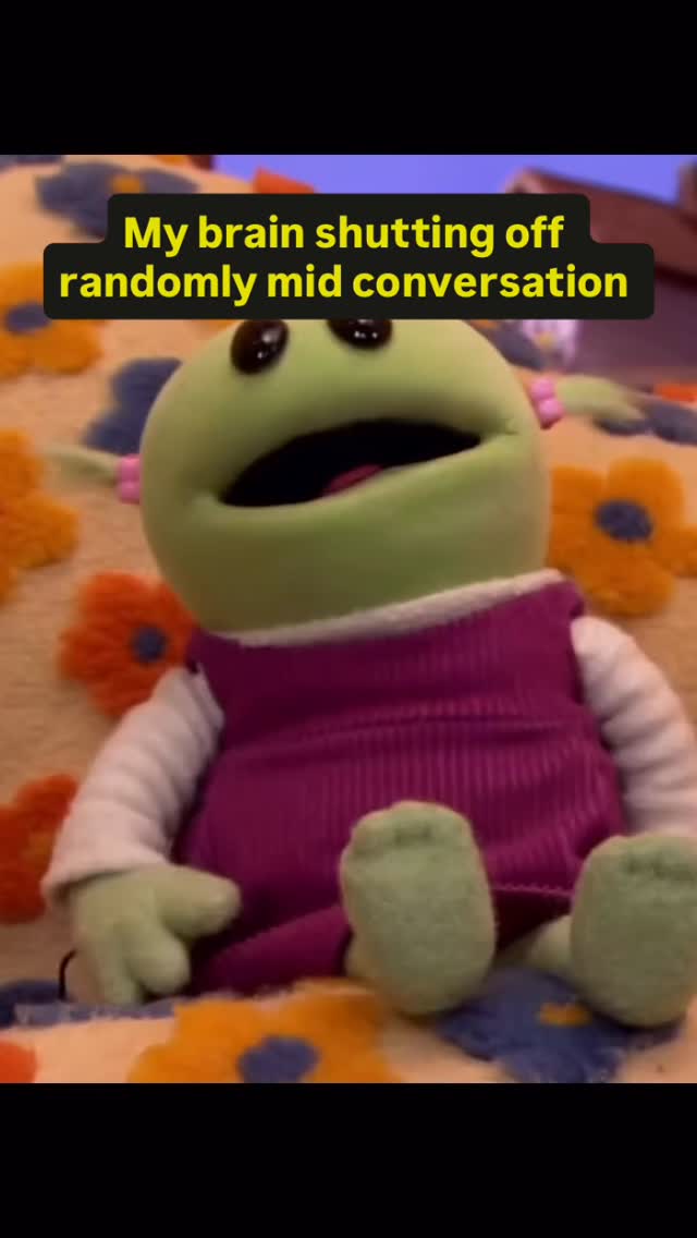 The image features a green felt puppet with large black eyes, a wide open mouth, and small green arms. The puppet is wearing a purple vest over a white shirt. The background has a colorful, patterned fabric with a flower-like design. Text overlaid in a black box says, "My brain shutting off randomly mid conversation."