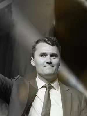 A grayscale portrait of a man in a suit and tie, viewed from the chest up. The man has short, neatly styled hair and a serious expression. The background is blurred, creating a soft focus that emphasizes the man's features. The lighting is such that it appears to be in a studio.