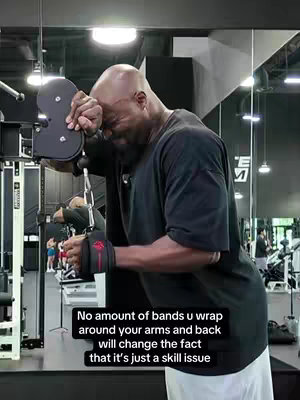 A man with a bald head and black t-shirt is featured, leaning and resting his head on a gym machine. In the foreground, the machine's arms and cables are in view, with the band on his wrist and upper arm. The background includes gym equipment and people working out. The image has a neutral color palette of black and white with a text overlay.