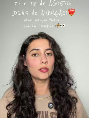 A woman with long, dark, wavy hair looks directly at the camera. She has makeup on, including blush and lipstick. The background is a solid, light gray. Above her head, text is overlaid in white handwritten-style font. The text includes dates and astrological terms, and a heart emoji. There is also a small badge on her shirt.
