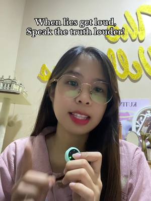 A young woman with long dark hair and glasses is centered in the frame, speaking directly to the camera. She is wearing a pink top. There is a text overlay at the top of the image. The background is a light wall with yellow decorations.