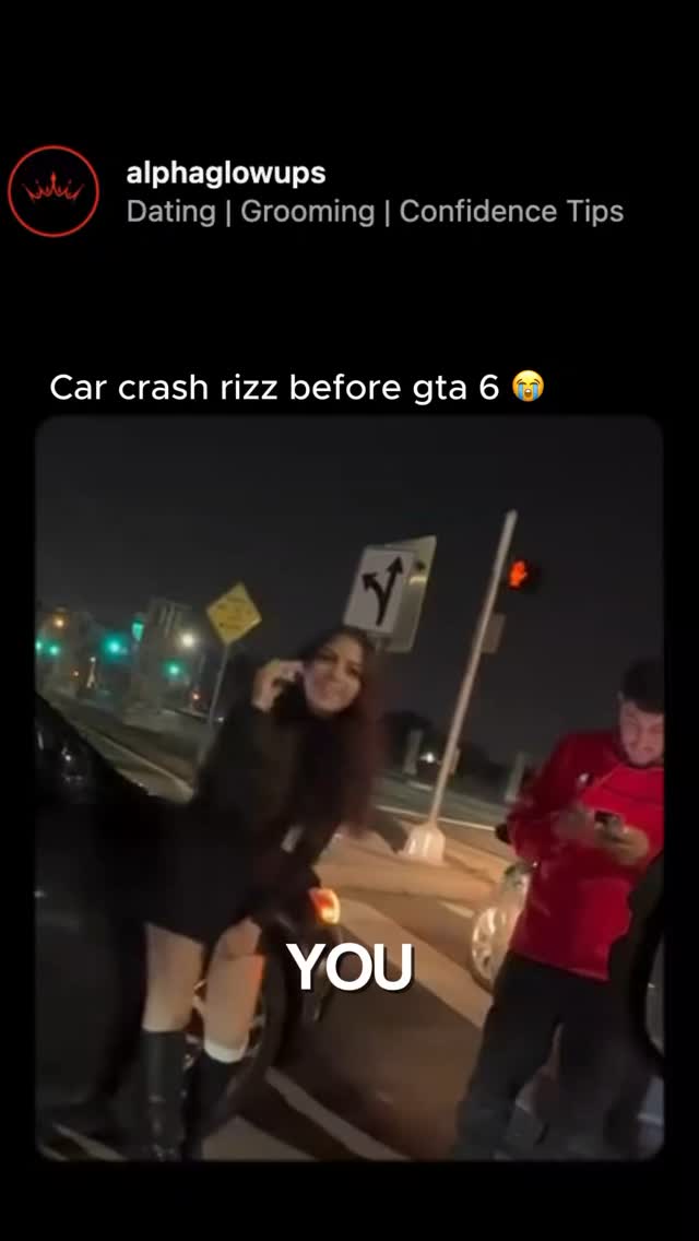 The image captures a nighttime scene of a street, possibly after a car accident. A woman stands near a car, holding a phone to her ear and appearing to be talking. Another man is present near the background of the car looking at his phone. A sign with an arrow pointing to the right is visible as well.