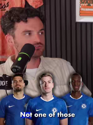 The image shows a man holding a microphone, with three soccer players superimposed in the foreground. Text at the bottom reads "Not one of those". The background is partially obscured by the man, with what could be clothing or posters visible.