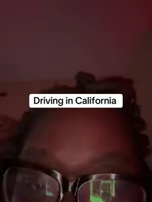 The image shows a close-up view, likely filmed from inside a car. The primary focus is on the creator, with the text overlay reading 'Driving in California'. The lighting is dim and warm.