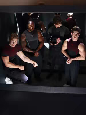 The cover image shows a mirror with a group of young men posing in workout attire. They are dressed in a black and maroon color scheme. One is kneeling, flexing his arm as if posing; the others are standing, and all are flexing. The lighting is balanced, making the group stand out against a darker backdrop.