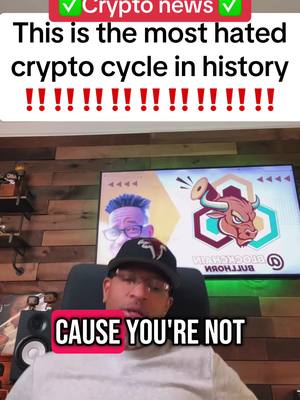A man wearing a black cap and glasses sits in an office-like setting. Behind him, a large screen displays a graphic with a bull and the words "Blockchain Bullhorn." Text overlays include "Crypto news" with checkmarks, along with other text and exclamation points.