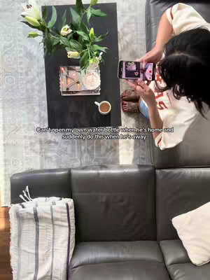 An overhead shot shows a woman holding a phone, likely taking a photo or video, with a cup of coffee, flowers, and decorations on a table. The text overlay explains the context of the video clip.