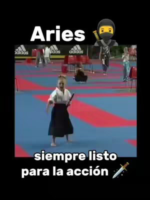 The cover image is a video still featuring a young girl in aikido attire, holding a katana. The background portrays an indoor sporting event with other athletes. The text overlay features the word 'Aries' in a bold, white font above, and the phrase 'siempre listo para la acción' (always ready for action) in a similar font below. A ninja emoji and a sword emoji are also added.