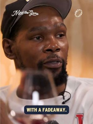 The image shows a close-up of a man, presumably Kevin Durant, wearing a black cap and a white t-shirt with a red 'T' on it. The background is blurred. Overlay text at the bottom reads, 'WITH A FADEAWAY.' The Mind the Game and Uninterrupted logos are also present.