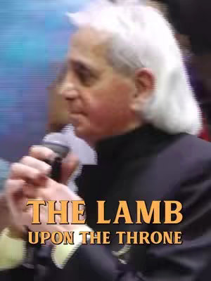 A man with gray hair and a dark suit is holding a microphone, with text overlayed at the bottom of the frame.