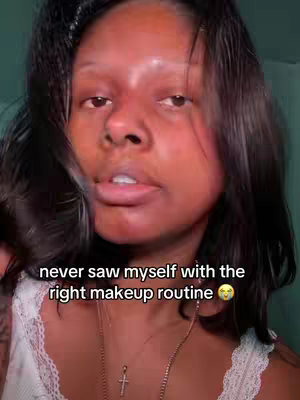 A close-up shot of a woman with dark hair, looking directly at the camera with a slightly open mouth. She is wearing a white top with lace detailing. Text overlayed on the image says 'never saw myself with the right makeup routine' with a shocked face emoji.
