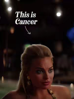 A close-up shot of a woman with blonde hair, looking downwards with a concentrated expression. The background is dark and blurred, adding focus to the woman. Text overlaid at the top states 'This is Cancer'.