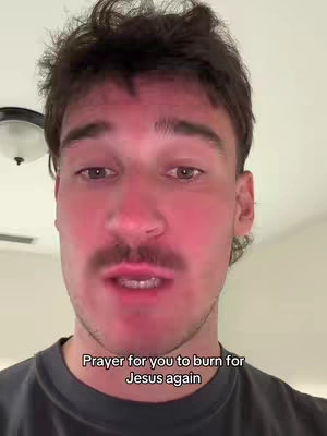 A close-up shot features a man with short, dark hair, a prominent mustache, and a slightly flushed complexion, possibly due to lighting or a skin condition. He is looking at the camera with a serious, slightly weary expression. Overlayed text at the bottom reads, 'Prayer for you to burn for Jesus again.' The background is indistinct, with a ceiling light partially visible.