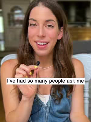 A woman with long brown hair is centered in the frame, looking toward the viewer and holding a small microphone in her left hand. She is wearing a light-colored top and a denim-like shirt. Overlay text, a white rectangular box with black font, across the bottom states I've had so many people ask me.