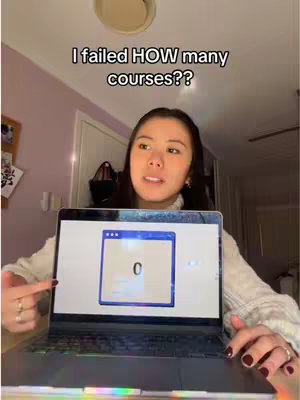 A young woman sits in front of a laptop, holding it up with both hands. Her face is centered in the frame, angled towards the camera as she speaks. The laptop screen displays a window with a blue border and the number '0' shown in a minimalist style. The background suggests an interior setting, with visible ceiling fixtures and a wall.