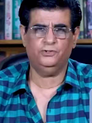 In the cover image, a man with dark hair and glasses is the central focus. He wears a blue and teal plaid shirt speaking towards the viewer. The background contains elements of an office.
