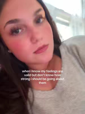 A close-up shot of a young woman with dark hair and fair skin. She is positioned slightly off-center, with her face illuminated by soft lighting. Her cheeks have a soft pink blush, and her lips are a natural pink. The background is blurred, giving emphasis to her expressive eyes.