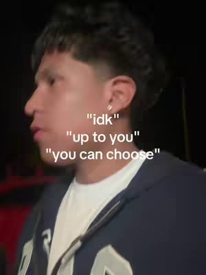 A young man with dark hair and a dark hoodie is standing in front of an indistinct background. White text overlays his face, with the phrases "idk", "up to you", and "you can choose".