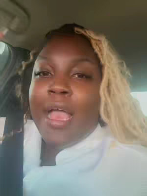 A selfie of a woman inside a car. She has dark skin, blonde hair, and is looking towards the camera with her tongue out.