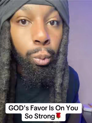 A close-up portrait shows a man with a dark complexion, dark dreadlocks, and a full beard. He has his mouth slightly pursed, as if about to speak or kiss. The background is blurred, featuring a purple hue. The words 'GOD's Favor Is On You So Strong' are displayed in a white rectangular box at the bottom, with a rose emoji at the end.