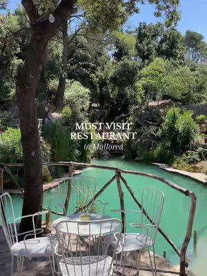 An outdoor scene featuring a restaurant beside a bright turquoise body of water, with trees and foliage in the background. The foreground shows a wooden railing supporting a few white metal chairs and a table. Overlayed text advertises the restaurant.