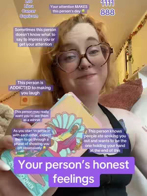 A selfie-style video cover image. A young woman with red hair, wearing heart-shaped glasses, is holding tarot cards. White text boxes with text relating to a person's feelings and attraction are placed around her face.