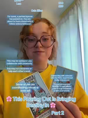 A woman with round glasses and a yellow sweater holds tarot cards, with overlay text describing a reading, against a background of a window with curtains. The composition is a selfie-style shot, with the woman centered and looking towards the camera.