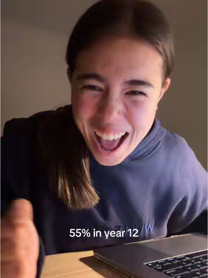 A young woman with dark hair is shown in a close-up shot, her face lit brightly as she looks directly at the camera with a wide, exaggerated expression. Her mouth is open in a broad smile or laugh, and her eyes are wide, conveying a sense of excitement or surprise. She is wearing a dark blue hoodie, and a laptop is partially visible in the bottom right corner. The background is dimly lit, which emphasizes the brightness of her face and the text overlay that provides context to the image.