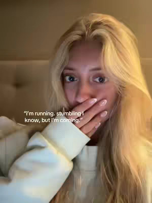 The cover image is a selfie featuring a young woman with long, wavy blonde hair. She is positioned in a well-lit indoor setting, likely her home, with warm lighting suggesting evening or a cozy atmosphere. She is wearing a light-colored sweatshirt. Her left hand is raised to cover her mouth, with the index and middle fingers gently resting on her lips. The background is lightly blurred, focusing attention on the woman's face and expression, highlighting her blue eyes. The overall composition employs soft lighting and a close-up perspective, drawing the viewer's focus to the woman's face, with a contemplative tone.