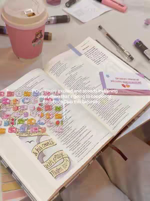 The image is a close-up, well-lit shot taken from a high-angle perspective, focusing on a Bible opened on a table. The composition includes a pink coffee cup, writing utensils, and various stickers, all set on what appears to be a light-colored wooden surface. The open Bible with decorative text, a quote, and a pink cup with a character on it dominating the view. The overall mood is calm with soft, saturated colors.