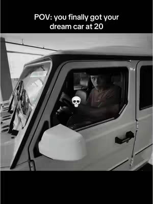 A grayscale POV shot inside a white SUV. The creator sits behind the wheel, looking towards the camera. A skull and crossbones sticker is on the steering wheel. The text overlay reads, 'POV: you finally got your dream car at 20'.