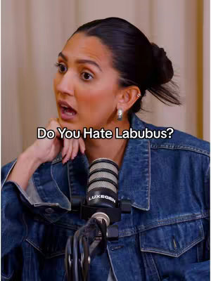 A woman with dark hair in a bun is positioned slightly off-center, looking up and to her left with an open mouth as if speaking or reacting. She is wearing a denim jacket and her dark hair is pulled back into a bun. A microphone with a LuxeGen logo is positioned below her face. The image uses a warm color palette, with soft lighting.
