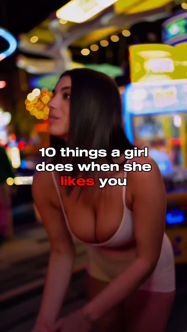 A woman in a white top is the central focus of the image, which seems to be taken in a vibrant environment. The background is blurred, but the edges of what seems to be an arcade setting are visible, with bright lights and potential game machines. The woman is slightly angled, and the text overlay is placed directly over the image.