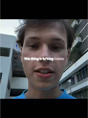 A selfie-style shot of a young man with short hair, wearing a blue shirt, with a building in the background. Text overlayed in neon-like white font across the man's face, and he appears to be looking at the camera.