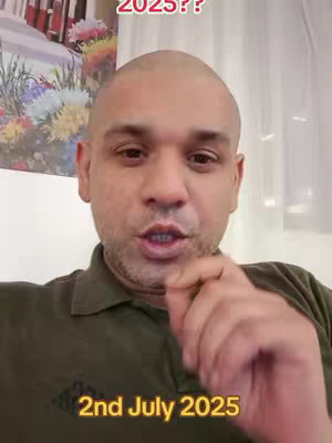 A medium close-up shot of a man with a shaved head, framed from the chest up. He has a neutral skin tone, and is speaking. The background includes a floral arrangement and curtains. Text overlays in yellow say '2025??' at the top and '2nd July 2025' at the bottom.