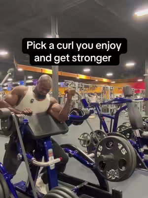 A man in a tank top performs a preacher curl in a gym. The image is centered on the man with the barbell in the foreground and gym equipment in the background. Text overlay in black, and orange.
