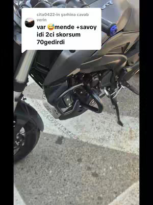 The image is a close-up shot of a motorcycle, specifically focusing on its front and side. The motorcycle is black, and the shot is taken outdoors. A speech bubble is overlaid on the image containing text. The background has a blurry appearance.