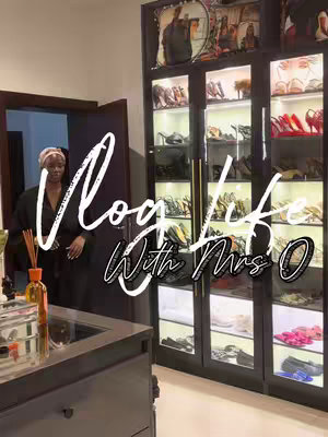 The image displays a woman standing in her walk-in closet, which is filled with shoes and accessories. The woman is wearing a black robe and a headscarf. The text overlay reads 'Vlog Life With Mrs O'