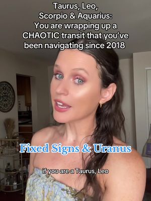 A woman stands in a well-lit indoor space, with a neutral background that includes interior decor. The woman has shoulder-length dark hair, wears a light, patterned top, and is speaking. Overlayed text reads 'Fixed Signs & Uranus' and further text at the top explains astrological concepts.
