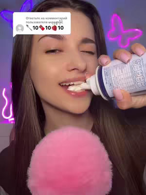 A young woman is seen in a close-up, holding a tube of whipped cream towards her mouth. She is about to eat some of the cream. The background is blurred and pink with neon lights, including a butterfly and two other shapes. There's a speech bubble with text to the upper left of her over a white square.
