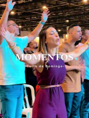 A group of people with their arms raised in what looks like worship or praise. The main figure is a woman wearing a purple dress. Text overlayed on the cover image says "Momentos - Culto de Domingo". The image is generally well-lit and appears to be taken in a church setting.