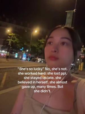 A woman is walking on a street at night, with buildings and streetlights in the background. Text is overlaid on the image with a quote regarding someone's hard work and perseverance.