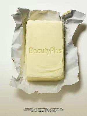 A top-down shot presents a block of butter inside a partially unwrapped silver foil wrapper, set against a white backdrop. The butter is pale yellow, with the text "BeautyPlus" embossed on its surface. The foil wrapper is open, with the edges crumpled. Below, there is a block of text.