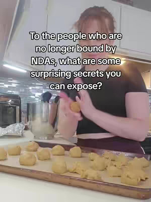 A person is in a kitchen setting. In front of them on a baking sheet, there are many circular pieces of dough. The person's hands are actively handling more dough in a rolling motion.
