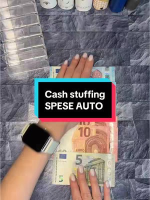 The image shows a person's hands arranging euro banknotes on a patterned dark background. A text overlay in a black and colored block reads "Cash stuffing SPESE AUTO". The person is wearing a watch. Beside the person's hand is a clear plastic container.