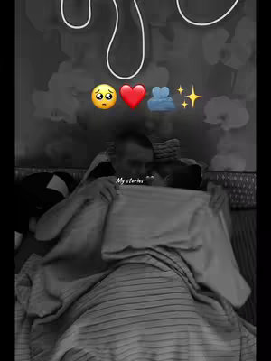 The image is a grayscale, vertical-oriented shot of a couple lying in bed. The top of the image features a white design element. Above the couple, there are several emojis and sparkles in a row. At the bottom of the image there's the text 'My stories'.