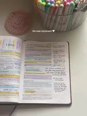 The image showcases an open bible with notes and highlighted text, along with various colorful pens in a clear container on a white surface. A decorative pink coaster is also present. The text overlay reads "the new testament 🩷".